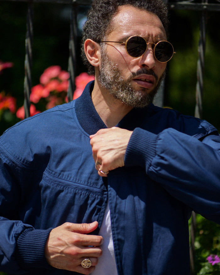 Man wearing a blue jacket and sunglasses with a blurred background of flowers