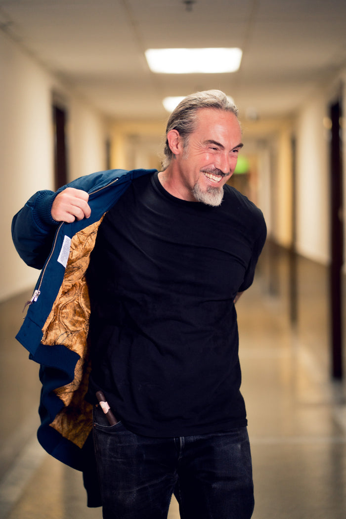 Man in a hallway holding a blue jacket with a fur lining